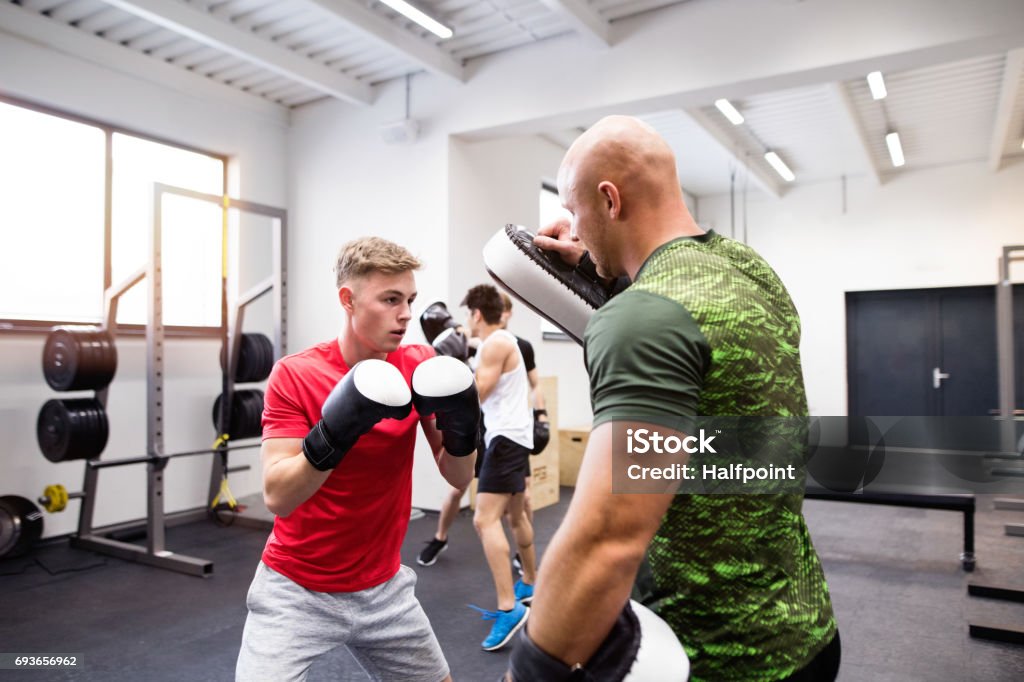 Handsome fit young man in gym boxing with his trainer. Handsome fit young man boxing with his personal trainer. Athlete boxers wearing boxing gloves sparred in boxing gym. Active Lifestyle Stock Photo