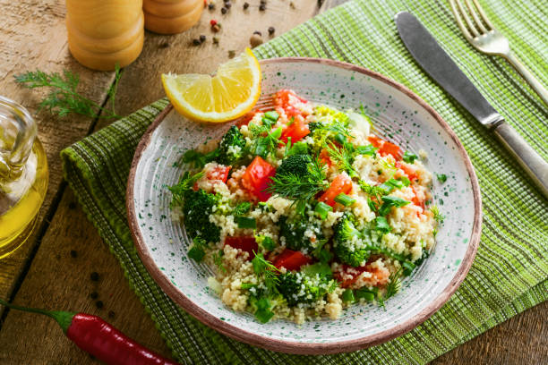 Traditional eastern couscous with broccoli, tomato, pepper, onion and dill on a plate for healthy meal. Moroccan healthy food on a table. Top view.