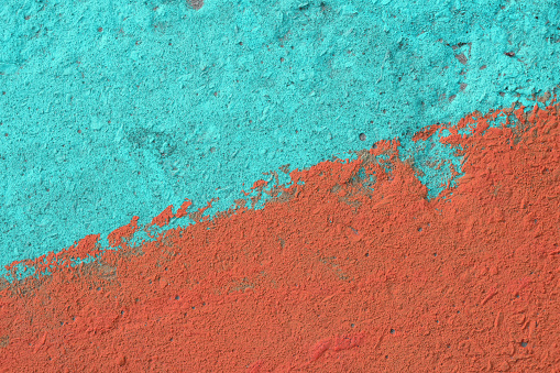 Vivid teal blue and coral orange painted rough concrete wall or floor texture background close up with diagonal color split in the middle