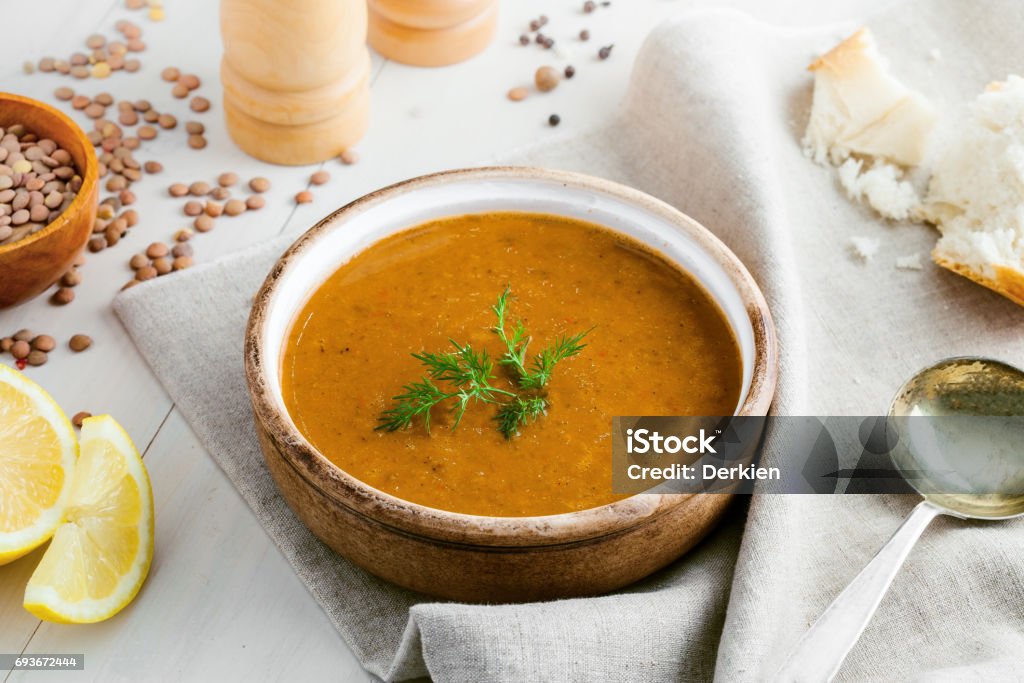 Lentil soup in a rustic bowl Bowl of delicious lentil soup with bread and lemon slice on a white wooden table. Traditional healthy vegetarian food. Top view. Soup Stock Photo