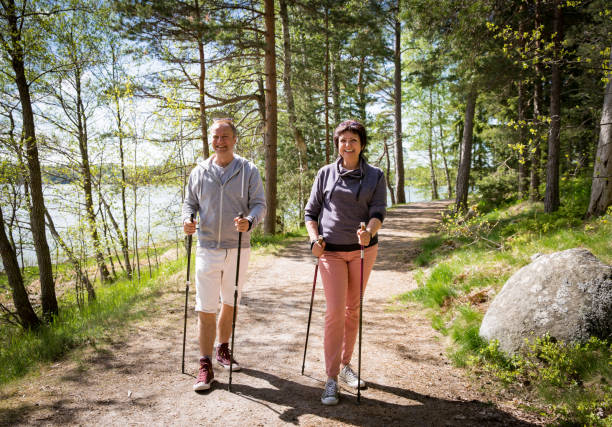 Summer sport in Finland - nordic walking Summer sport in Finland - nordic walking. Man and mature woman hiking in green sunny forest. Active people outdoors. Scenic peaceful Finnish summer landscape. northern european stock pictures, royalty-free photos & images