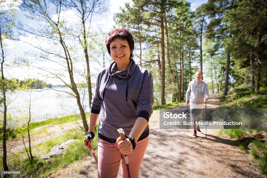 Summer sport in Finland - nordic walking Summer sport in Finland - nordic walking. Man and mature woman hiking in green sunny forest. Active people outdoors. Scenic peaceful Finnish summer landscape. Walking Stock Photo