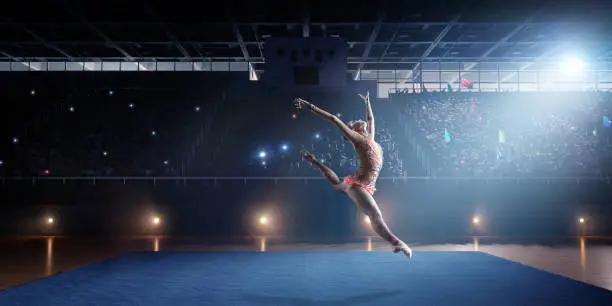 Photo of A gymnast girl makes a leap on a large professional stage