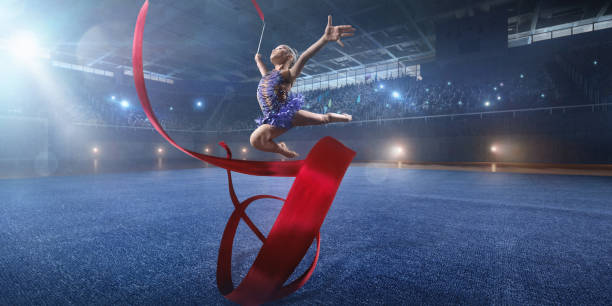 a small gymnast girl makes performance with gymnastic band on a large professional stage - concentration flexibility full length healthy lifestyle imagens e fotografias de stock