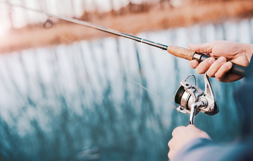 Close up photo of fisherman hands. Fisherman angling on the river. Fisherman standing on the riverside and trying to catch a bass. Sport, recreation, lifestyle