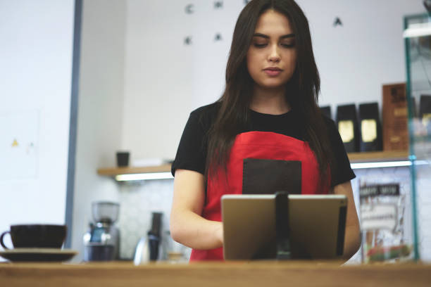 Attractive female businesswoman barista owner of bar caffe Confident young female cashier making ordering via tablet connected to wifi in cafe indoors counting bill, charming serious waitress using application for checking finance information of incomes caffe machine stock pictures, royalty-free photos & images