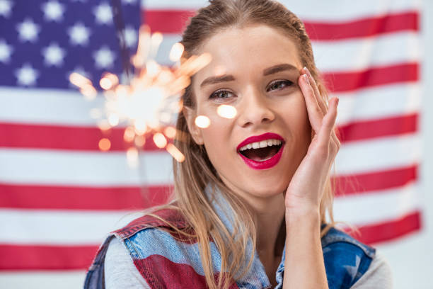 portrait of happy woman holding sparkler with american flag behind - independence spark fire flame imagens e fotografias de stock