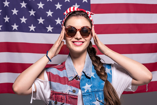 portrait of smiling stylish woman in sunglasses with american flag behind