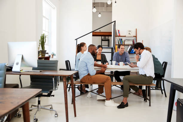 istock Creative team meet at a table in an office, one using phone 693724616