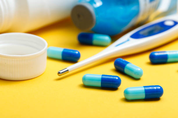 istock electronic thermometer and blue capsules on yellow background 693741028