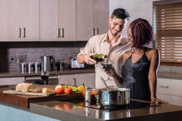 happy young mixed race couple cooking a meal in kitchen pasta wine stock photo