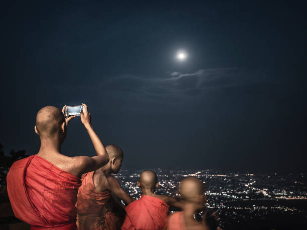 Buddhist monks looking at the full moon at Wat Phra That Doi Suthep the night before Wisaka Bucha in Chiang Mai Thailand. This temple in the outskirts of the city located on the top of a mountain that overlooks the city is a Theravadada Wat was founded in 1383. The Gautama Buddha's shoulder bone is supposed to be housed here as a relic. The night before Vesak or Buddha birthday and enlightenment day thousands of people do a pilgrimage to this temple to celebrate the most important day for buddhists. The festivity takes place on the full moon day of the sixth lunar month.