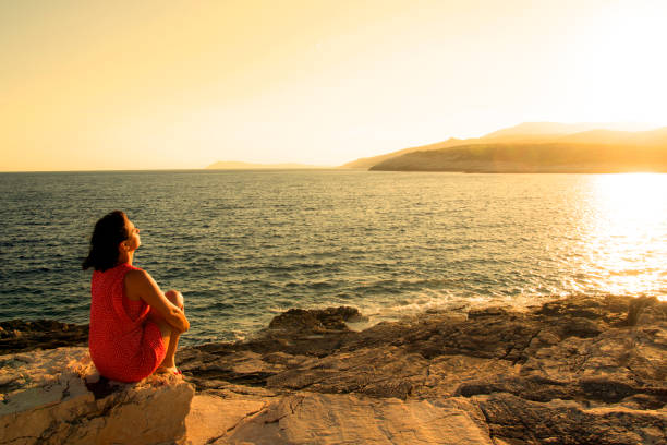 istock Woman sitting alone on rocks looking at view 693774864