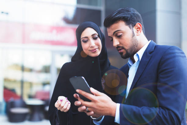 Modern Arab husband showing his wife an online message on his smart phone Modern Arab husband and wife after work in the Middle East. west asian ethnicity stock pictures, royalty-free photos & images
