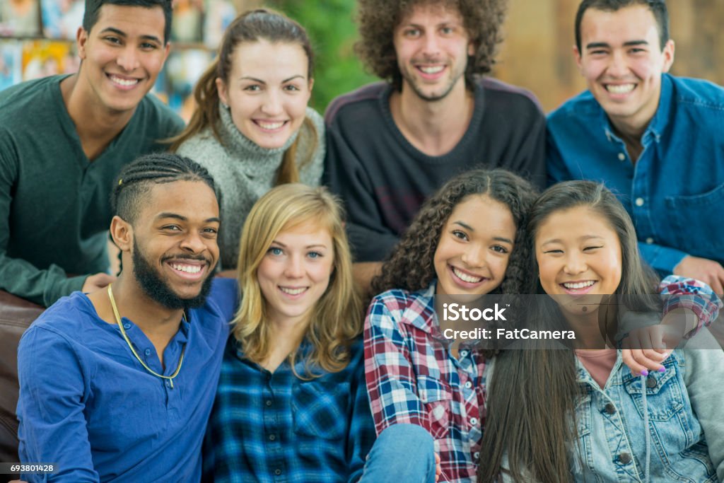 University Friends Hang Out in the Dorm A multi-ethnic group of young college students hug and smile in a big group as they look at the camera. They are in a cozy living room inside a dorm. 20-29 Years Stock Photo
