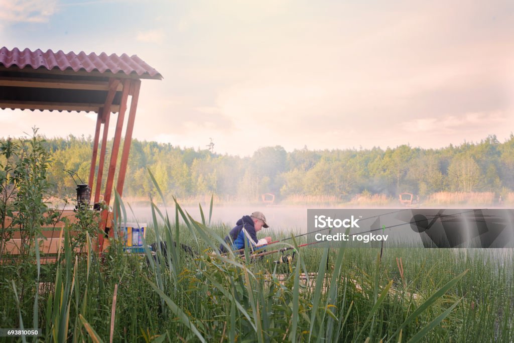The boy catches fish early in the morning on the river. Adult Stock Photo