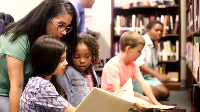 Education. brarian reads book to elementary students in library or classroom.