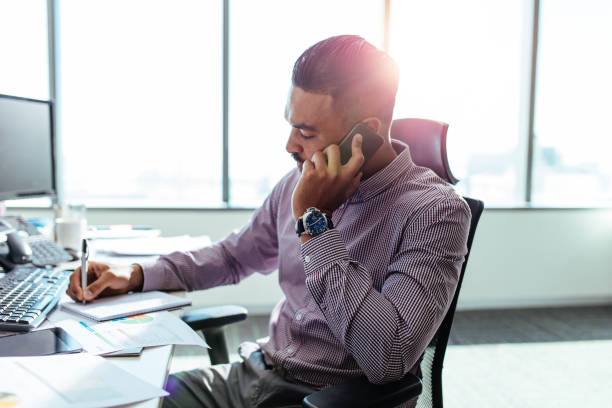 istock Businessman talking over mobile phone sitting at his office desk. 693830198