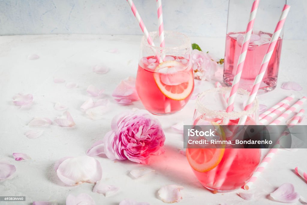 Light rose cocktail, rose wine Summer refreshment drinks. Light pink rose cocktail, with rose wine, tea rose petals, lemon. On a white stone concrete table. With striped pink tubules, petals and rose flowers. Copy space Cocktail Stock Photo