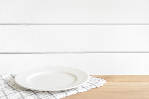 Empty white food plate put on wooden desk in white wood wall room.