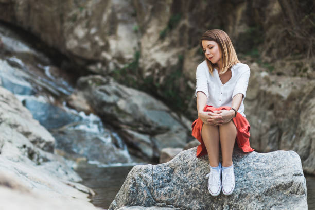 joven mujer sentada en la roca por el río - waterfall zen like women meditating fotografías e imágenes de stock
