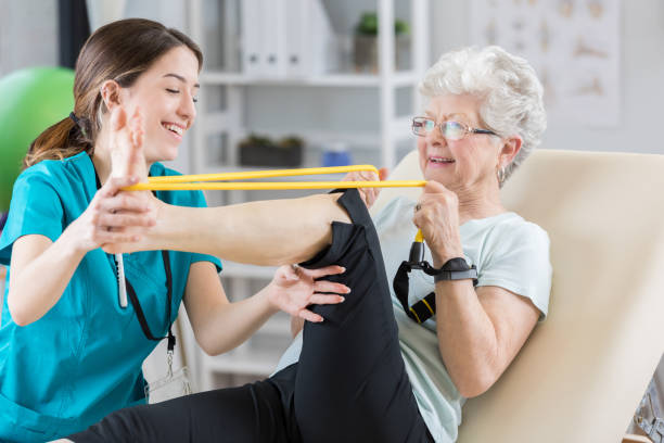 Physical therapist helps patient use resistance band Confident Caucasian female physical therapist helps senior Caucasian patient use resistance band. The woman is stretching out her leg. knee photos stock pictures, royalty-free photos & images