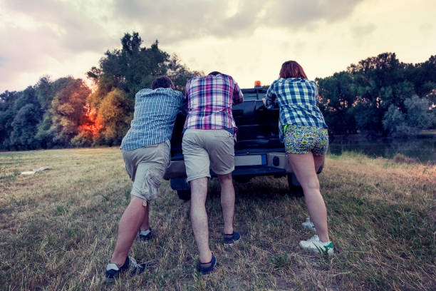 Group Of Friends Standing By Car On Coastal Road At Sunset