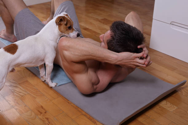 istock Muscular man doing abs exercises at home with dog watching him. 693884226