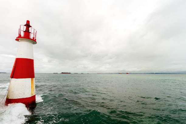Red and white lighthouse with freighter boats in background