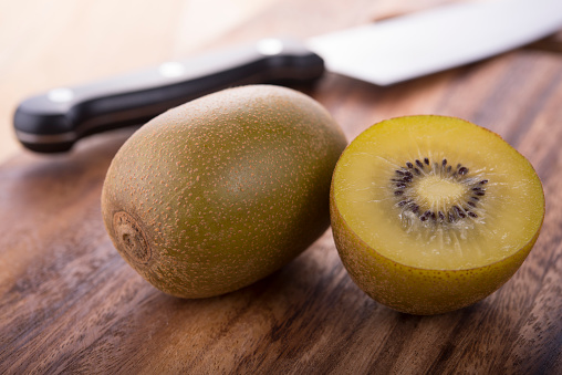 whole and half cut ripe golden kiwi with knife on cutting board