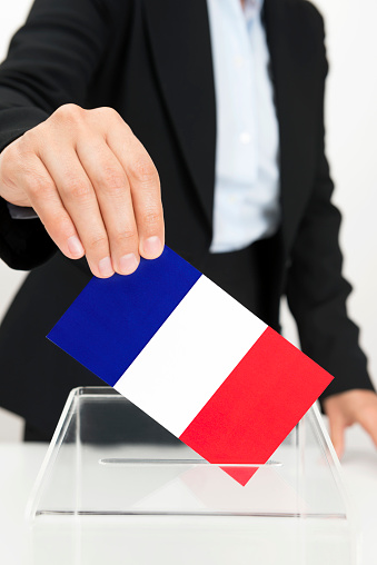 Human hand is inserting france flag into ballot box.