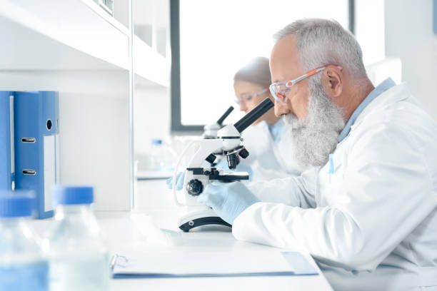 istock Side view of scientists in white coats working with microscopes in chemical lab 693992078