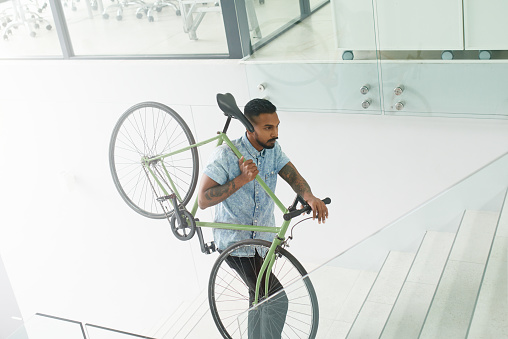 Shot of a young designer carrying his bicycle up a staircase in an office