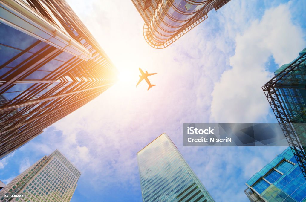 Airplane flying over modern business skyscrapers. Transport, travel. Airplane flying over modern business skyscrapers, high-rise buildings. Transport, transportation, travel. Sun light on blue sky. Airplane Stock Photo