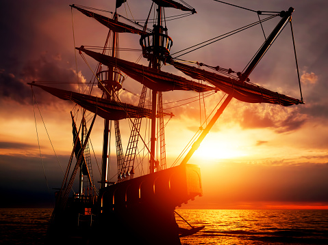 Old ancient pirate ship on peaceful ocean at sunset. Calm waves reflection, sun setting.