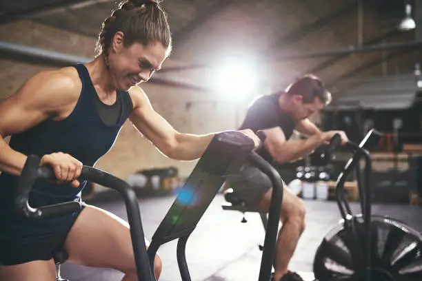 Sportive man and woman using equipment in spacious light gym and exercising hardly.
