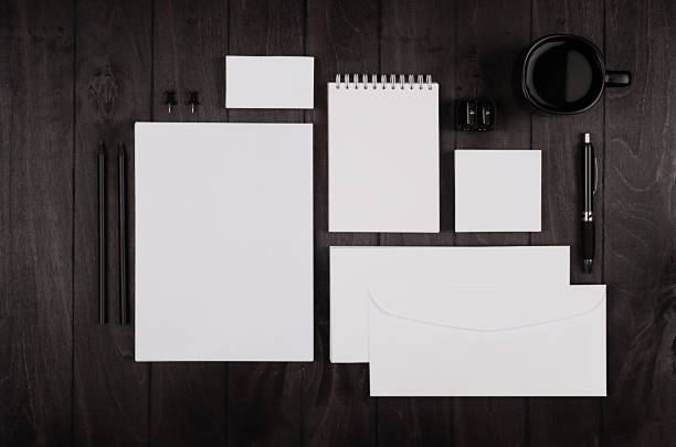 istock Dark elegance working space with blank notepad, letterhead, business card, coffee cup and earphone on black wood plank background. Template for your design. 694005276