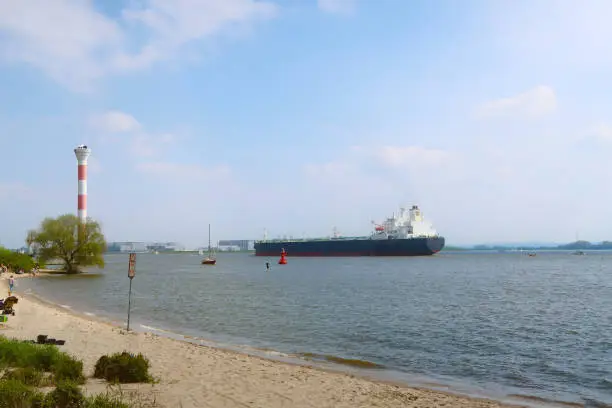 sandy beach on the river Elbe in Hamburg, Germany with large cargo ship passing by in background