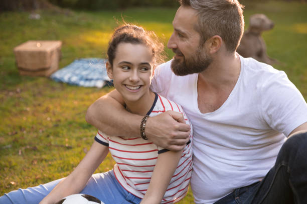 Smiling father embracing daughter on grassy field at park Smiling father embracing daughter on grassy field at park weimaraner dog animal domestic animals stock pictures, royalty-free photos & images