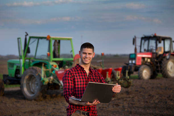 bauer mit laptop vor landwirtschaftliche geräte - farmer rural scene laptop computer stock-fotos und bilder