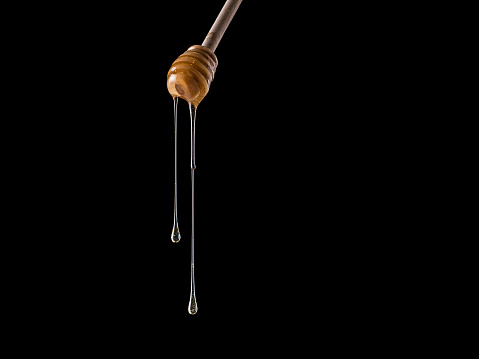 Organic honey flows from dipper. Isolated on black. Copy space. Honey stick with flowing honey
