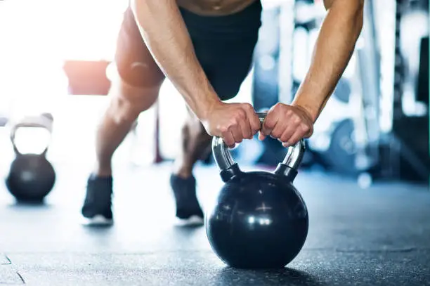 Photo of Unrecognizable fit man in gym doing push ups on kettlebells