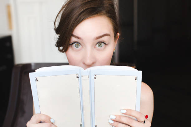 istock Surprised girl covers her face with a book 694054554
