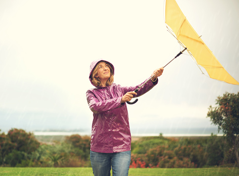 Shot of a woman standing outside in the rain holding an umbrella looking up in the sky