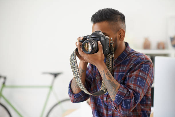 Shot of an unidentifiable young photographer holding his camera up to his face in the office