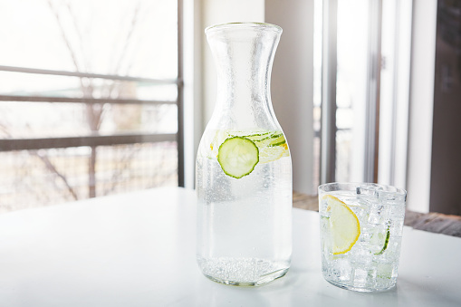 Shot of a jug and glass of water with slices of lemon and cucumber in