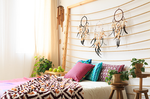 Bed with colorful blanket and pillows under bedheads with dreamcatchers