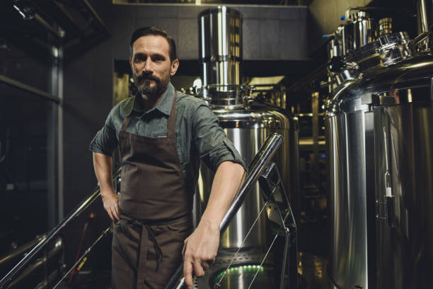 Male brewery worker in apron Male brewery worker in apron standing and looking at camera microbrewery photos stock pictures, royalty-free photos & images