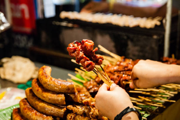 Man buys skewered grilled pork CHIANG MAI, THAILAND - AUGUST 27: Man buys grilled pork on skewers at the Sunday Market (Walking Street) on August 27, 2016 in Chiang Mai, Thailand. night market stock pictures, royalty-free photos & images