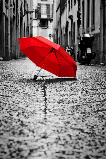 Red umbrella on cobblestone street in the old town. Wind and rain Red umbrella on cobblestone street in the old town. Wind, rain, stormy weather. Color in black and white conceptual, idea. Vintage, retro style. cobblestone photos stock pictures, royalty-free photos & images